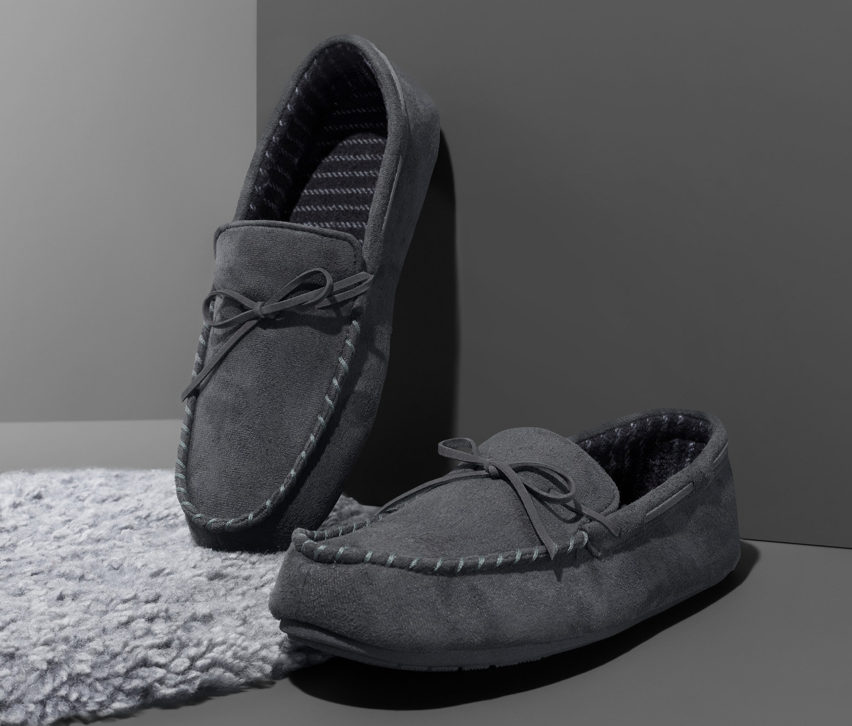 Zwei graue Hausschuhe stehen auf einem grauen Teppich vor einer grauen Wand.