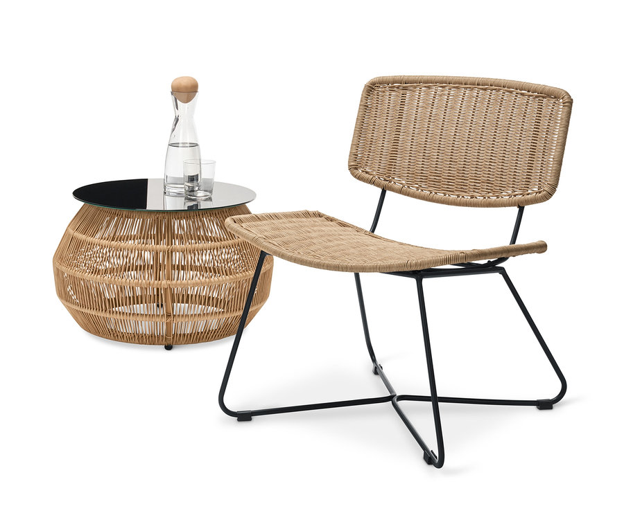 Ein Design-Loungesessel und ein Beistelltisch mit Polyrattangeflecht sind zu sehen. Auf dem Tisch stehen eine Karaffe Wasser und Gläser.
