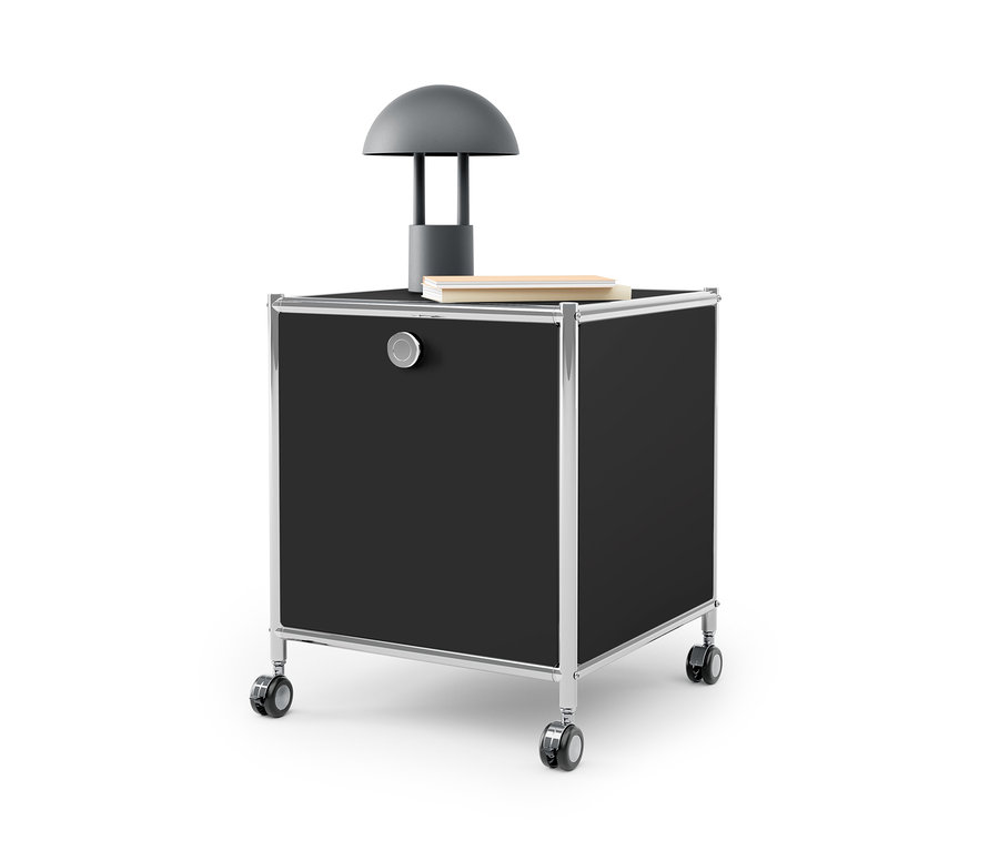 Ein schwarzer Beistelltisch mit Schublade Metall »CN3« mit silbernem Rahmen und Rädern. Auf dem Tisch stehen eine graue Lampe und ein Buch.