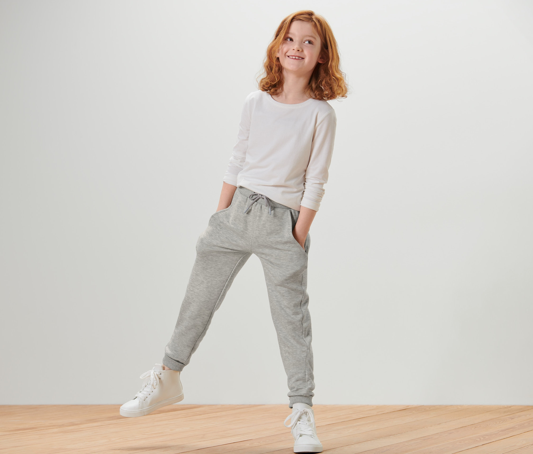 Mädchen mit weißem Langarmshirt und grau melierter Kinder-Sweathose.