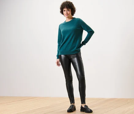 Frau posiert in grünem Pullover und Leggings in Lederoptik.