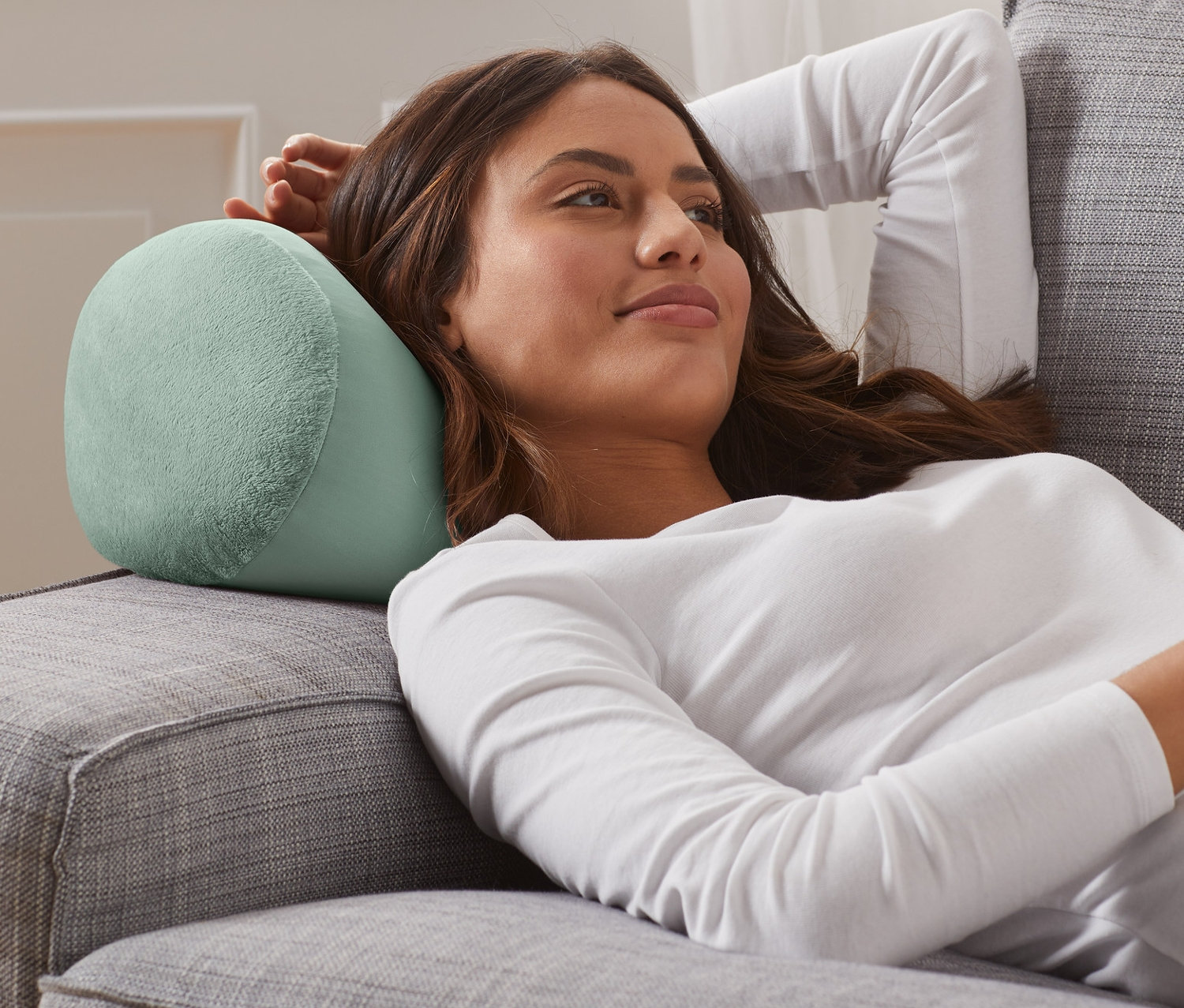 Frau liegt mit Relaxkissen auf einem grauen Sofa.