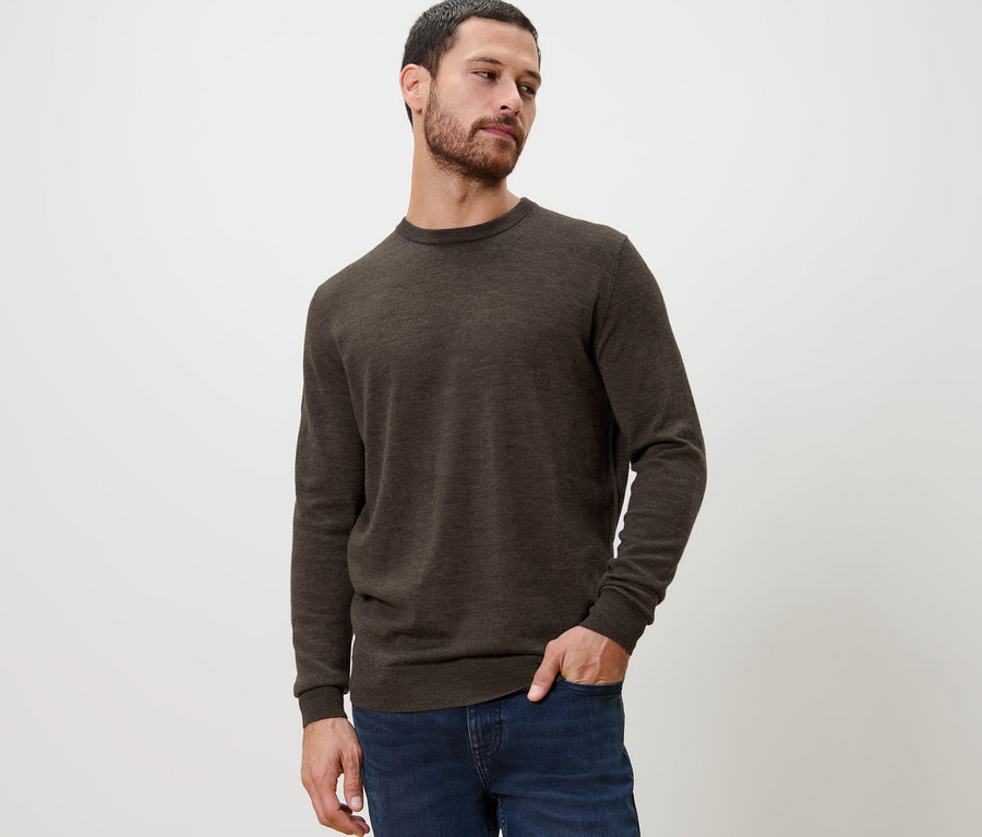 Mann posiert in braunem Merino-Pullover und Jeans.