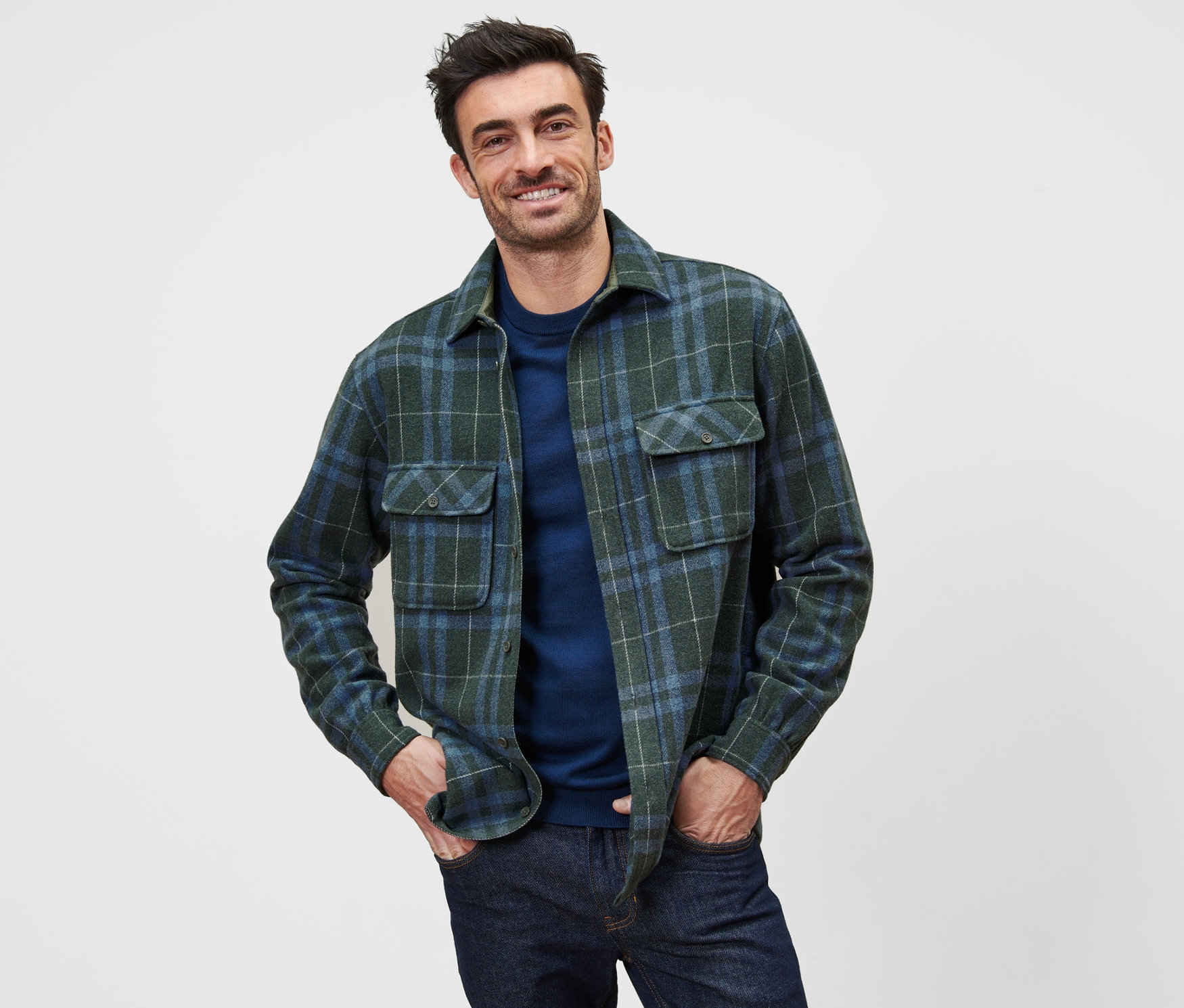 Mann posiert in einer grün und blau karierten Flanell-Hemdjacke.