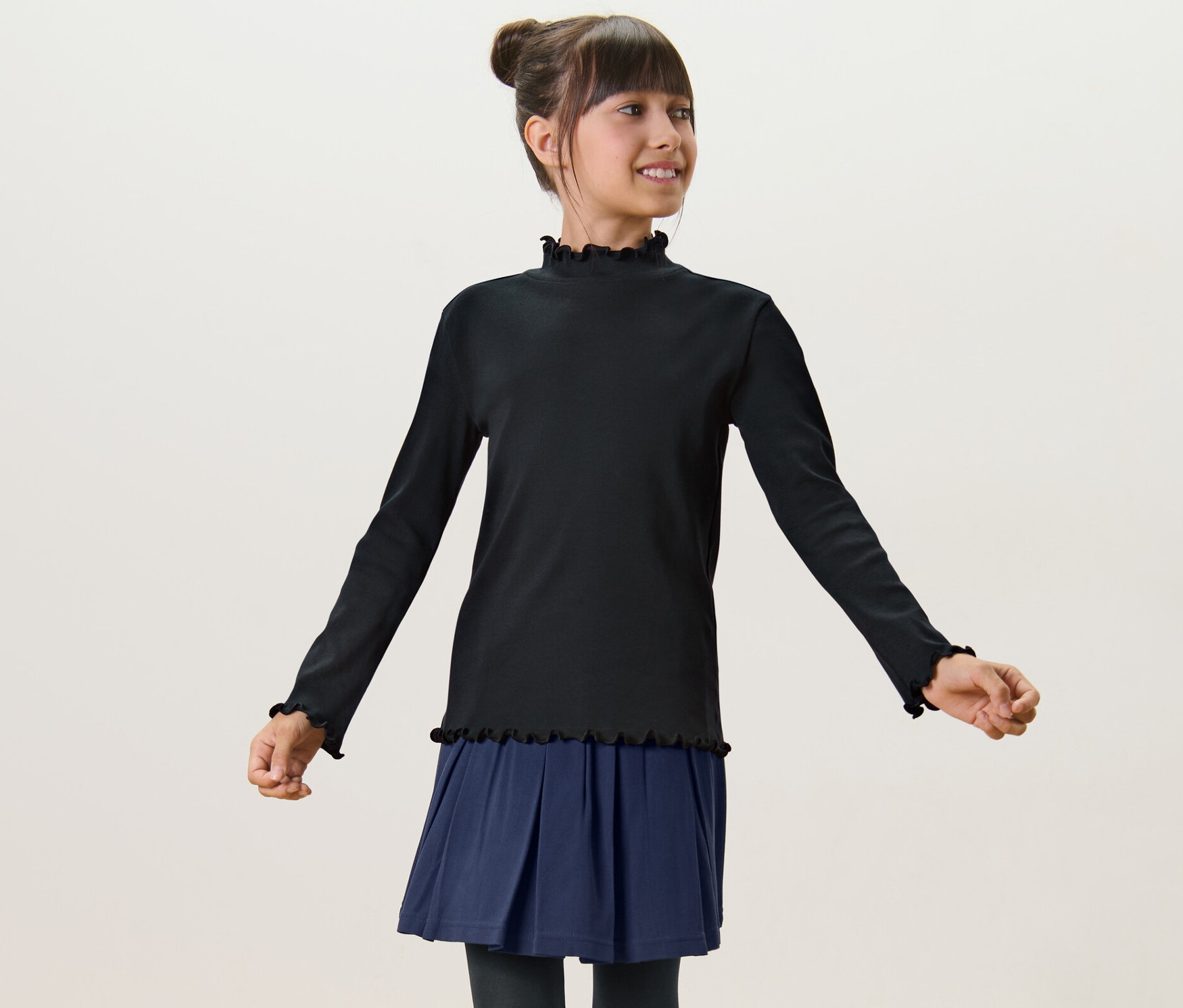 Mädchen trägt ein Kinder-Langarmshirt in Schwarz und einen blauen Rock.