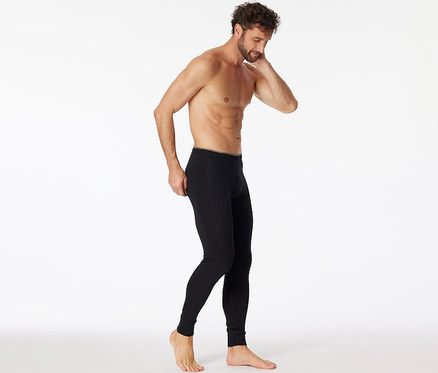 Mann, der eine schwarze SCHIESSER lange Unterhose mit Bio-Baumwolle trägt und sie an der Hüfte anpasst, während er nach unten blickt.