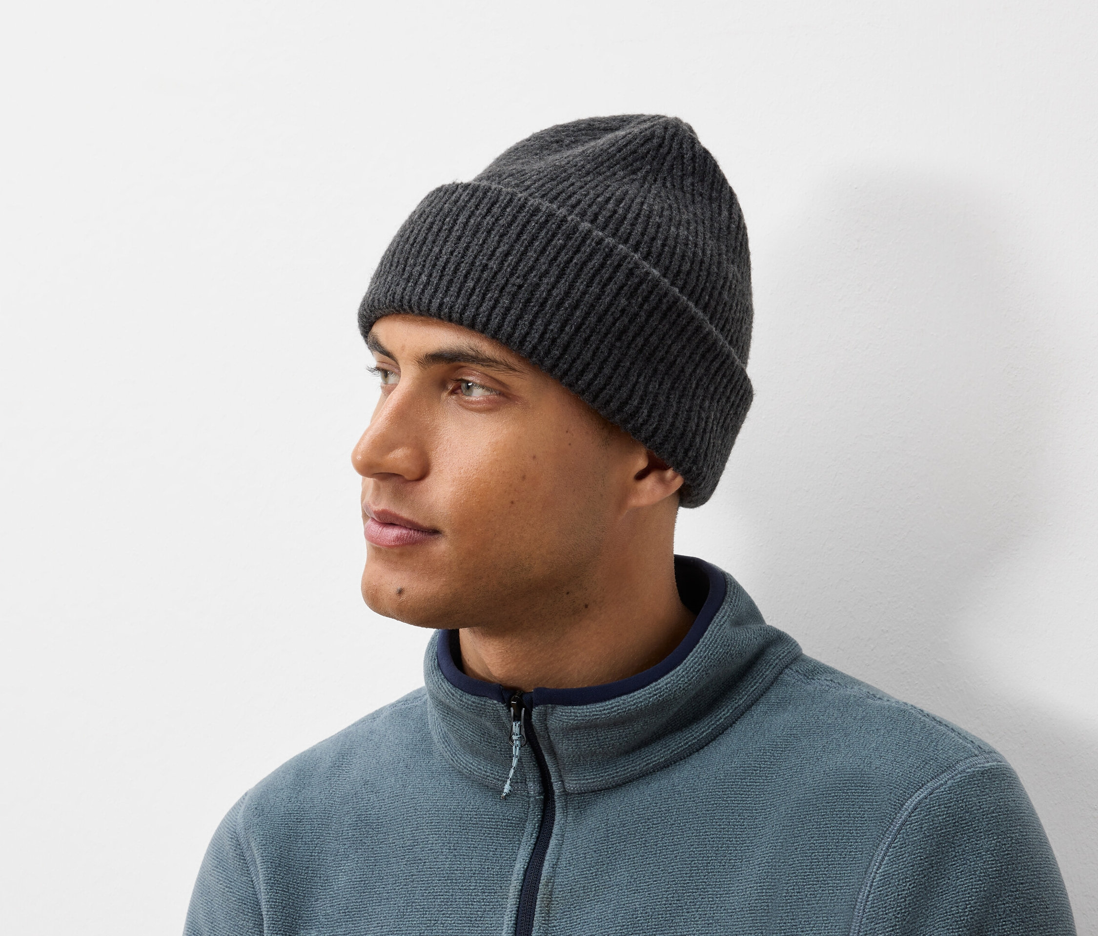 Porträt eines Mannes mit einer dunkelgrauen Strickmütze und einer blau-grauen Fleecejacke.