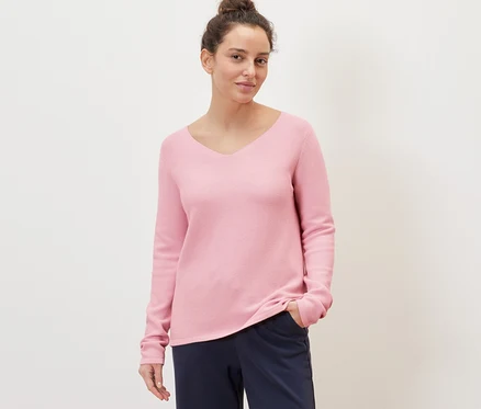 Frau posiert in einem rosafarbenen Strickpullover.