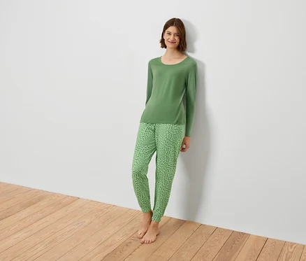 Frau im grünen Pyjama lehnt an einer weißen Wand.