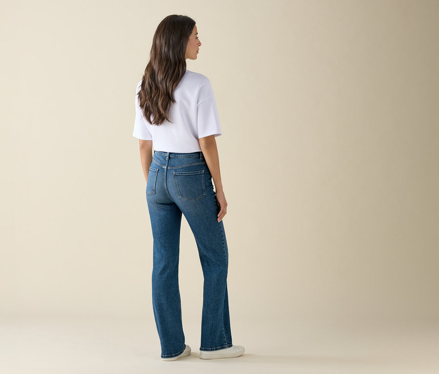 Frau steht mit dem Rücken zur Kamera, trägt blaue Jeans und ein weißes T-Shirt.