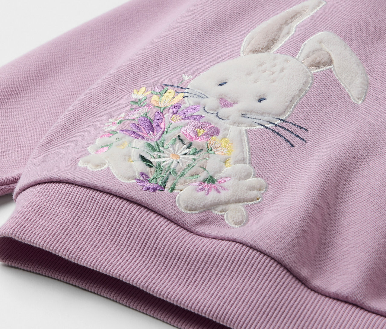 Detailansicht eines helllila Sweatshirts mit einer Applikation eines Hasen, der einen Blumenstrauß hält.