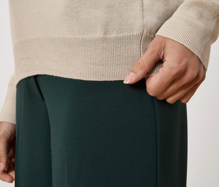 Detailaufnahme einer Person mit beigem Pullover und dunkelgrüner Hose.