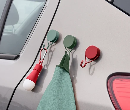 An der Seite eines Autos hängen drei farbige Haken, an denen ein Handtuch und eine Lampe befestigt sind.