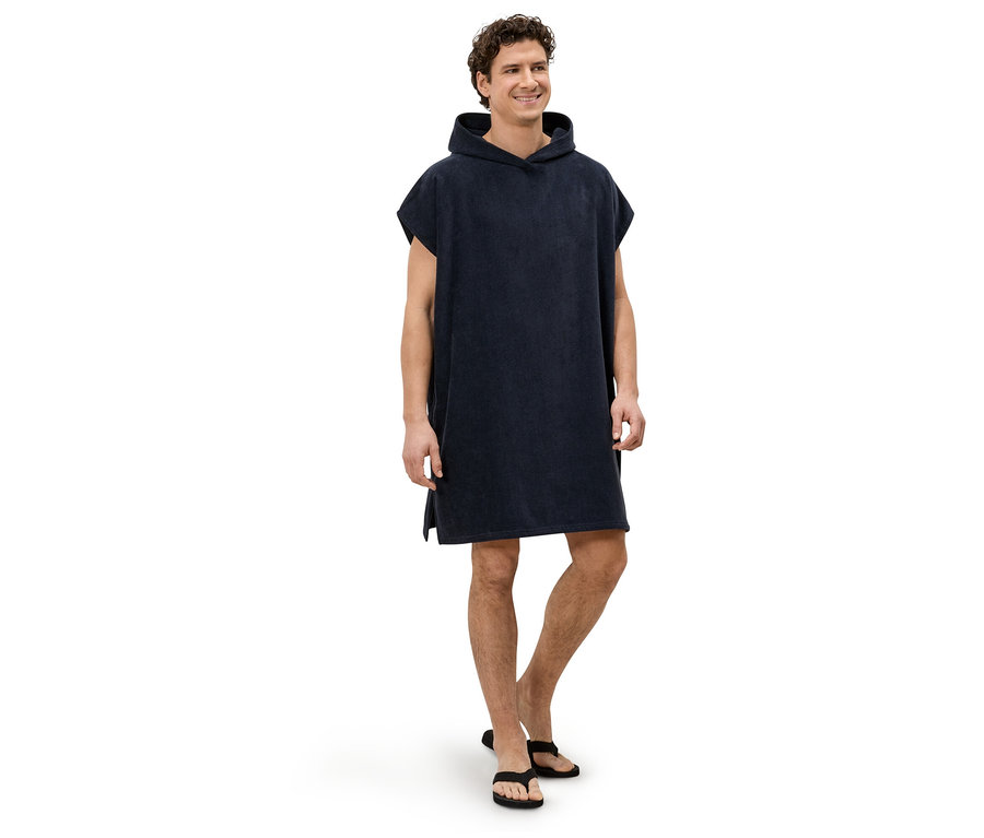 Ein Mann steht barfuß in einem marineblauen Kapuzenponcho und schwarzen Zehentrennern vor einem weißen Hintergrund.
