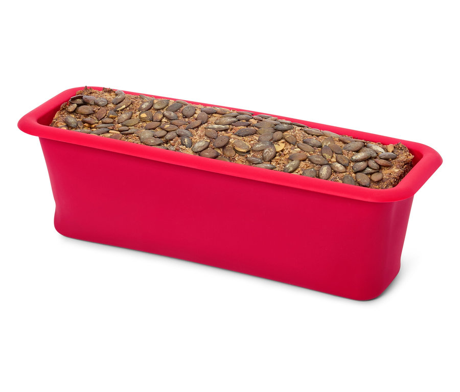 Ein roter Silikon-Brotkasten gefüllt mit einem Brot, das mit Kürbiskernen belegt ist.