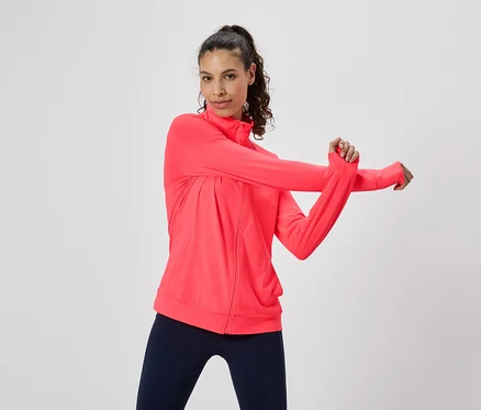 Frau dehnt sich in einer pinken Trainingsjacke und Leggings.