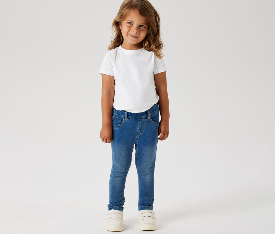 Mädchen trägt ein weißes T-Shirt und NAME IT Kinder-Jeggings und weiße Schuhe.
