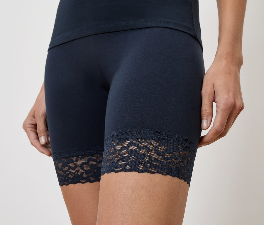 Nahaufnahme einer Frau, die marineblaue, kurze Leggings mit Spitzensaum und ein passendes Oberteil trägt.