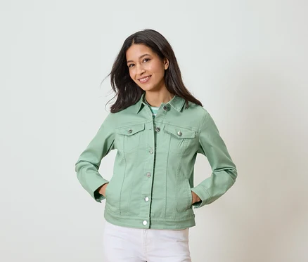 Frau mit hellgrüner Jeansjacke und weißen Hosen, die mit den Händen in den Taschen posiert.