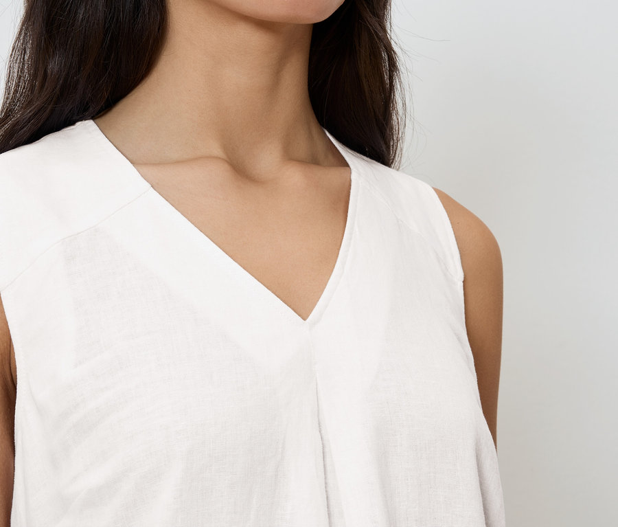 Nahaufnahme einer Frau, die ein ärmelloses, weißes V-Ausschnitt-Oberteil trägt.