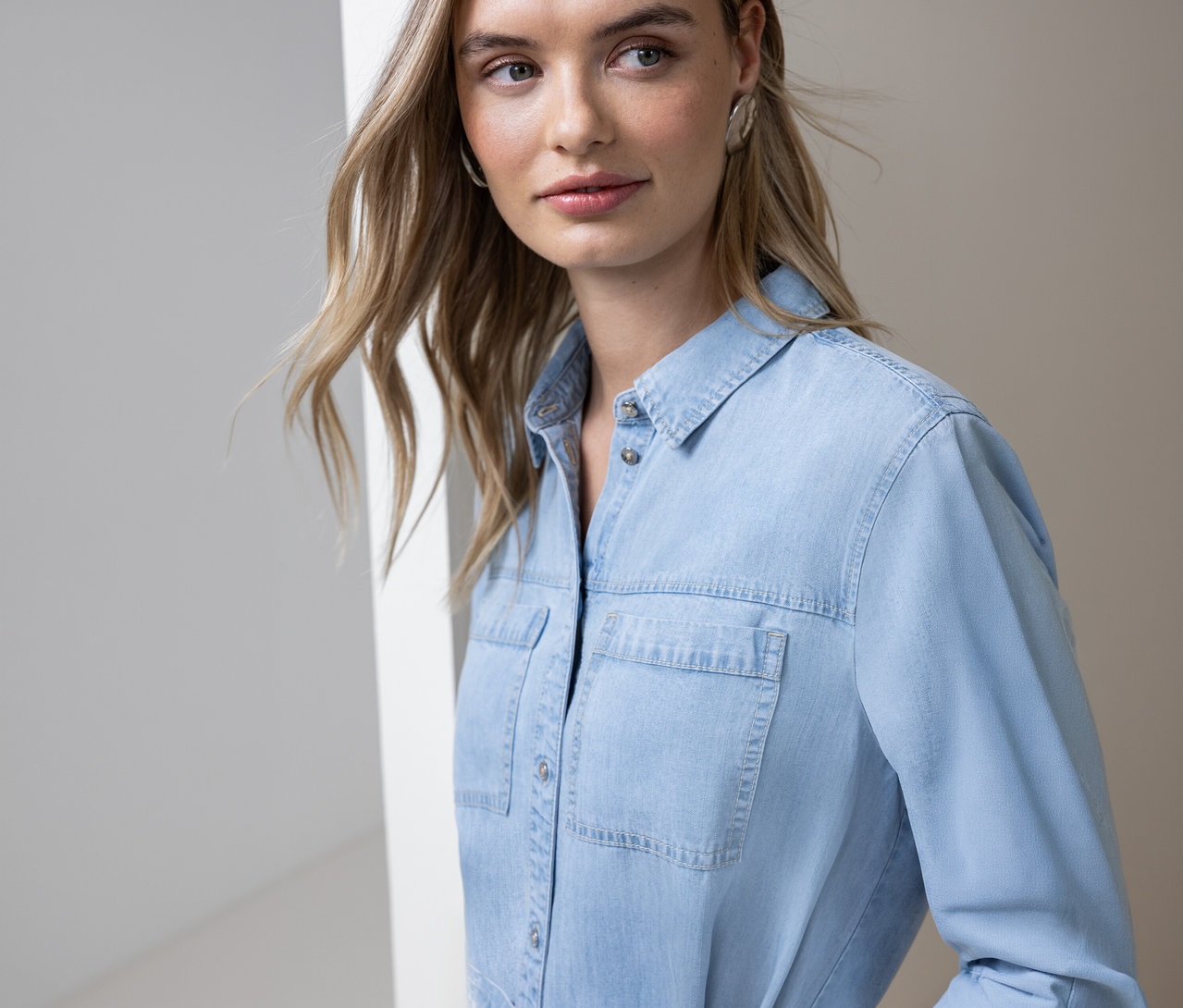 Frau mit blonden Haaren trägt ein hellblaues Jeanshemd mit Knöpfen und zwei Brusttaschen.