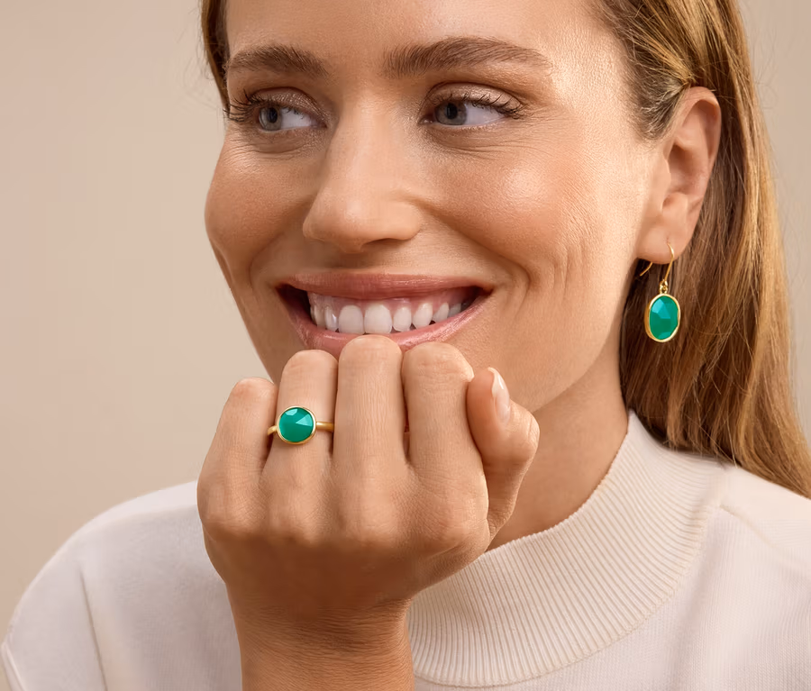 Lächelnde Frau mit Ring mit grünem Stein am Ringfinger und baumelnden Ohrringen mit grünem Stein.