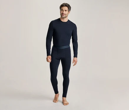 Mann in dunkelblauem, langärmeligem Thermoshirt und passender Thermoleggings, barfuß stehend und leicht lächelnd.