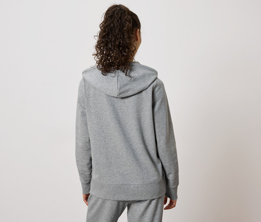 Rückansicht einer Frau mit lockigem Haar, die einen grauen Kapuzenpullover und eine Jogginghose trägt.
