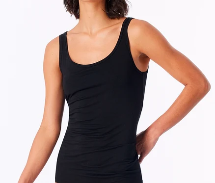 Eine Frau mit kurzen dunklen Haaren trägt ein schwarzes SCHIESSER Trägertop mit Modal vor weißem Hintergrund.