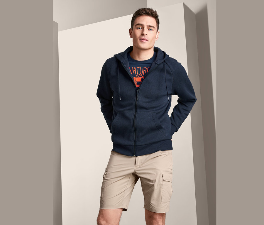 Mann trägt eine marineblaue Funktions-Sweatjacke und beige Shorts.