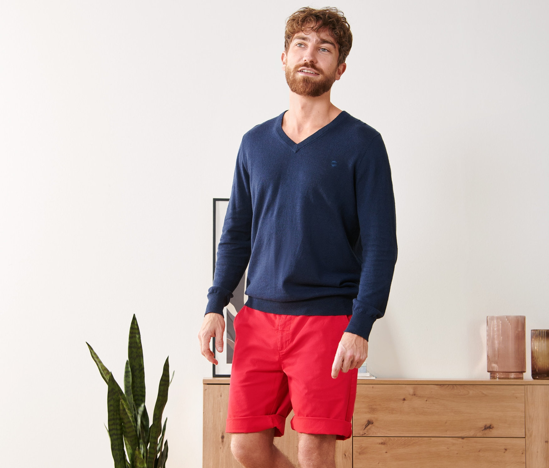 Mann trägt blauen Pullover und rote Chino-Shorts.