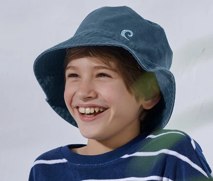 Ein lächelnder Junge sitzt mit einem blau-weiß gestreiften Oberteil und einem Kinder-Fischerhut.