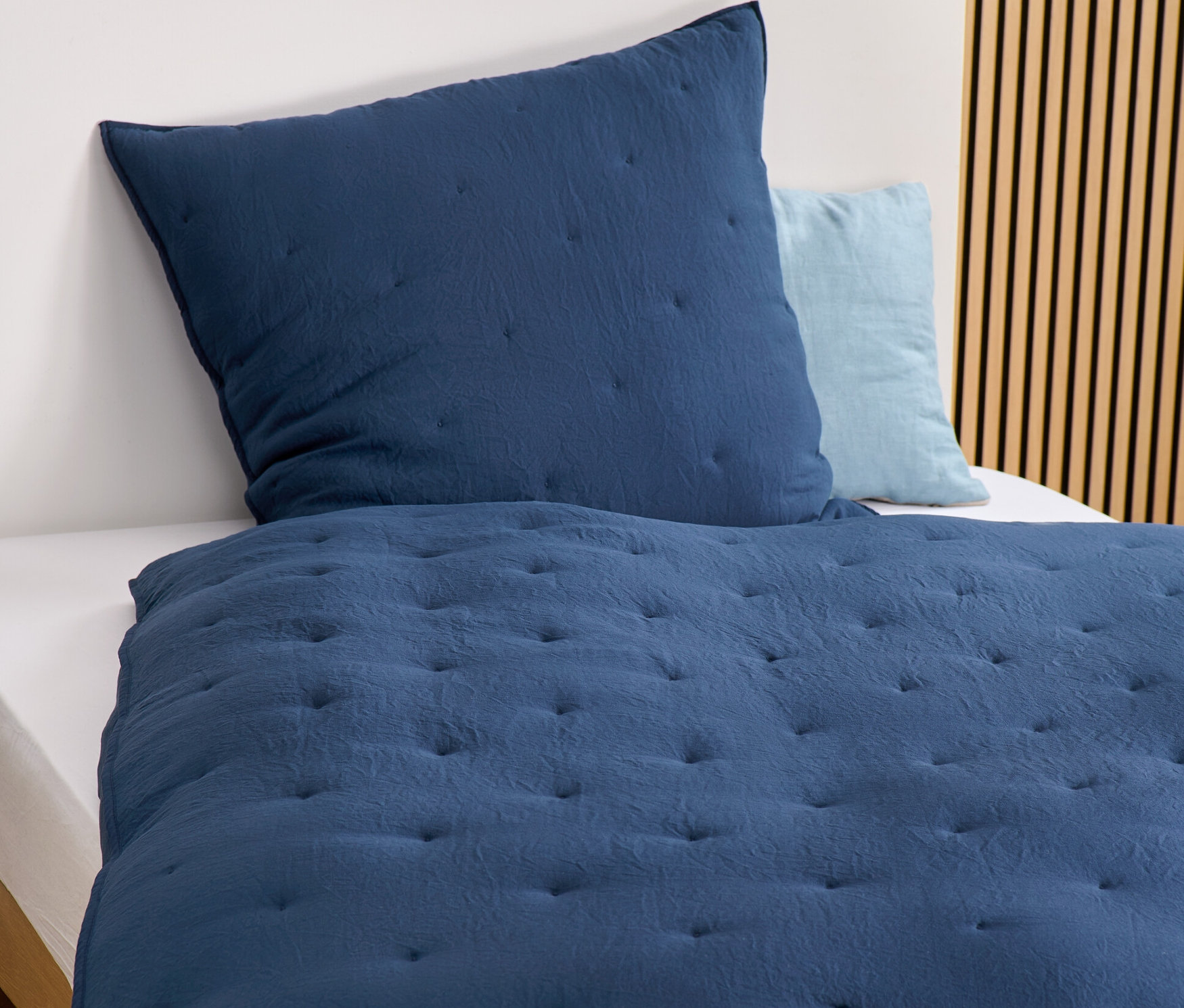 Detailansicht von marineblauer Bettwäsche mit Steppmuster und Kissen auf einem Bett.