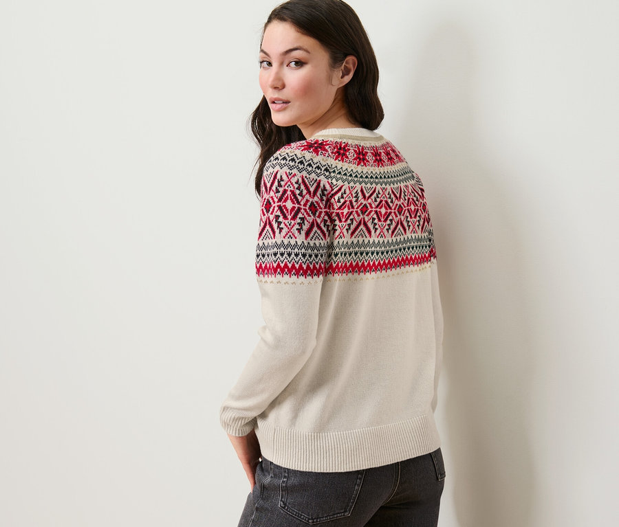 Frau blickt über die Schulter und trägt einen Norweger-Strickpullover und Jeans.