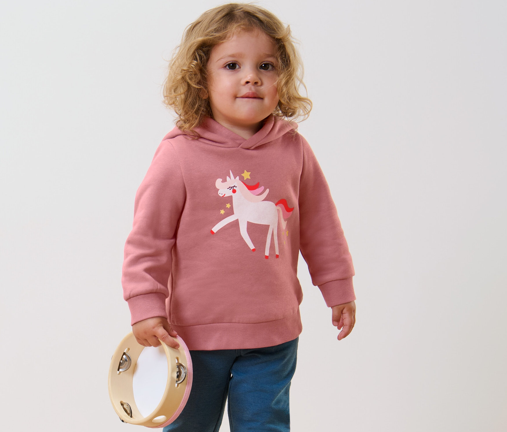 Kind mit Tamburin trägt ein Kinder-Sweatshirt mit Wendepailletten, Einhorn oder Print (Gr. 86/92).