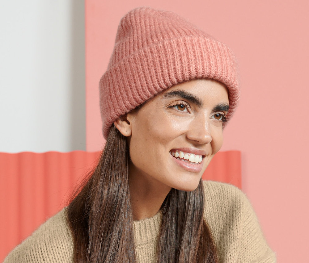 Frau sitzt auf einem Stuhl und trägt eine Strickmütze.