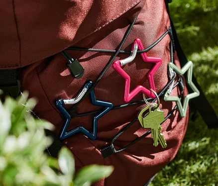 Drei verschiedenfarbige »Stern« Karabinerhaken sind an einem Rucksack befestigt.