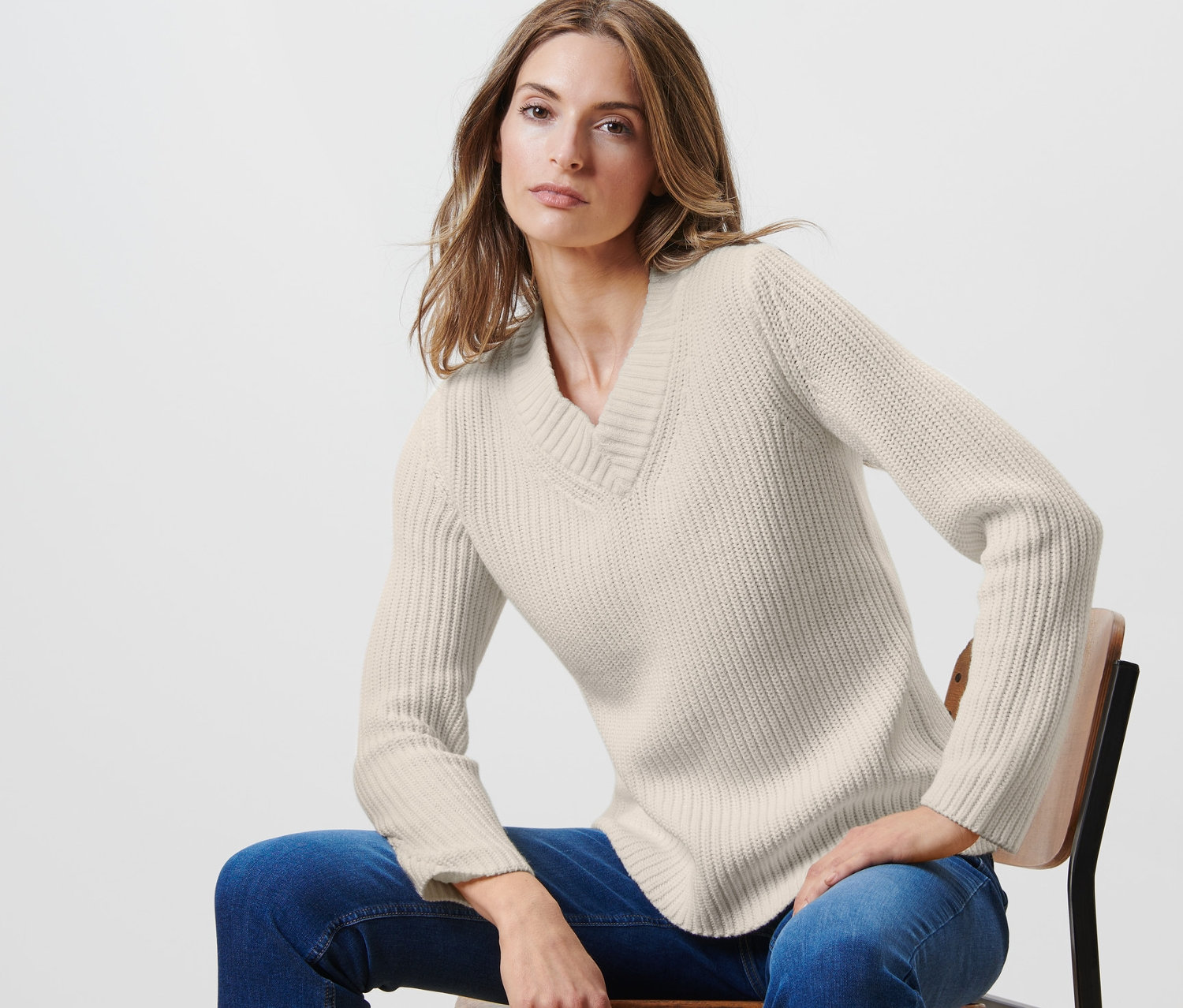 Frau sitzt auf einem Stuhl und trägt einen offwhite Strickpullover.
