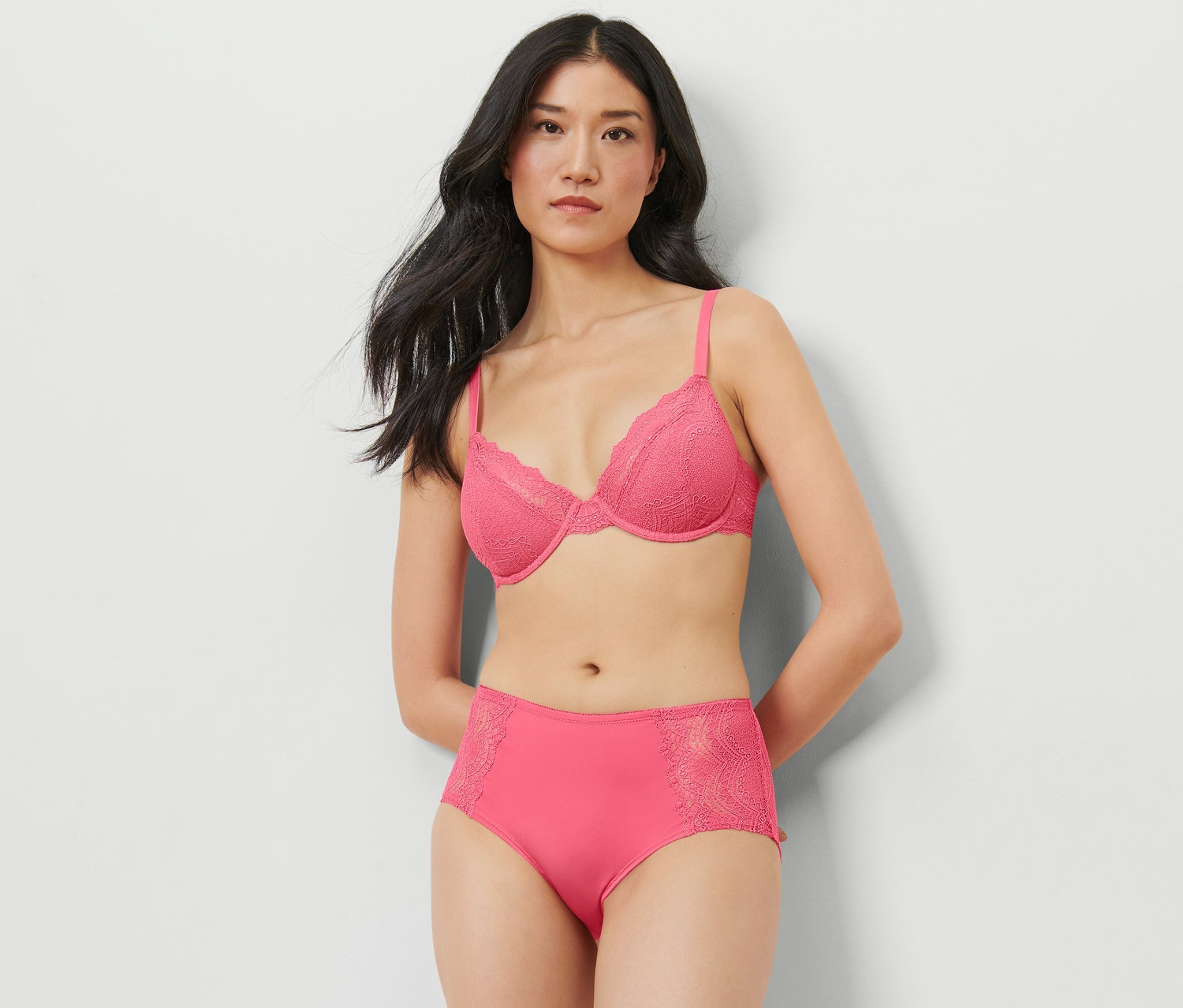 Frau posiert im Studio in einem pinkfarbenen BH und einer Midrise-Panty.