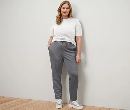 Eine Frau steht und trägt ein weißes Basic Halbarmshirt, ein dunkelblaues Basic Halbarmshirt, eine Joggpants und Plateau-Sneaker aus Leder.