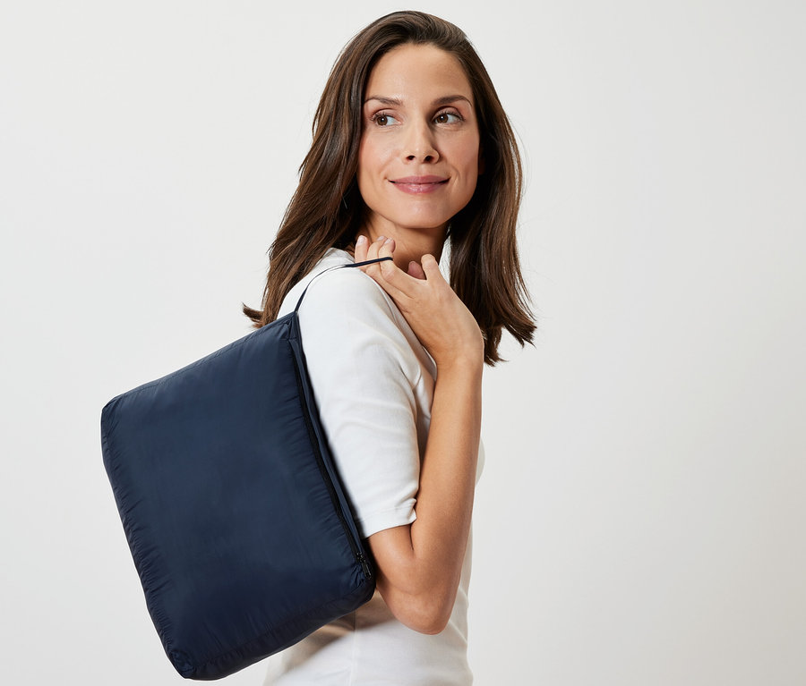 Frau mit dunkelblauer Reisedecke "Ultraleichte Reisedecke" über der Schulter.