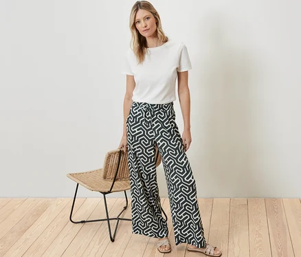 Eine Frau steht und trägt ein weißes T-Shirt und eine bedruckte Schlupfhose in Crinkle-Optik.