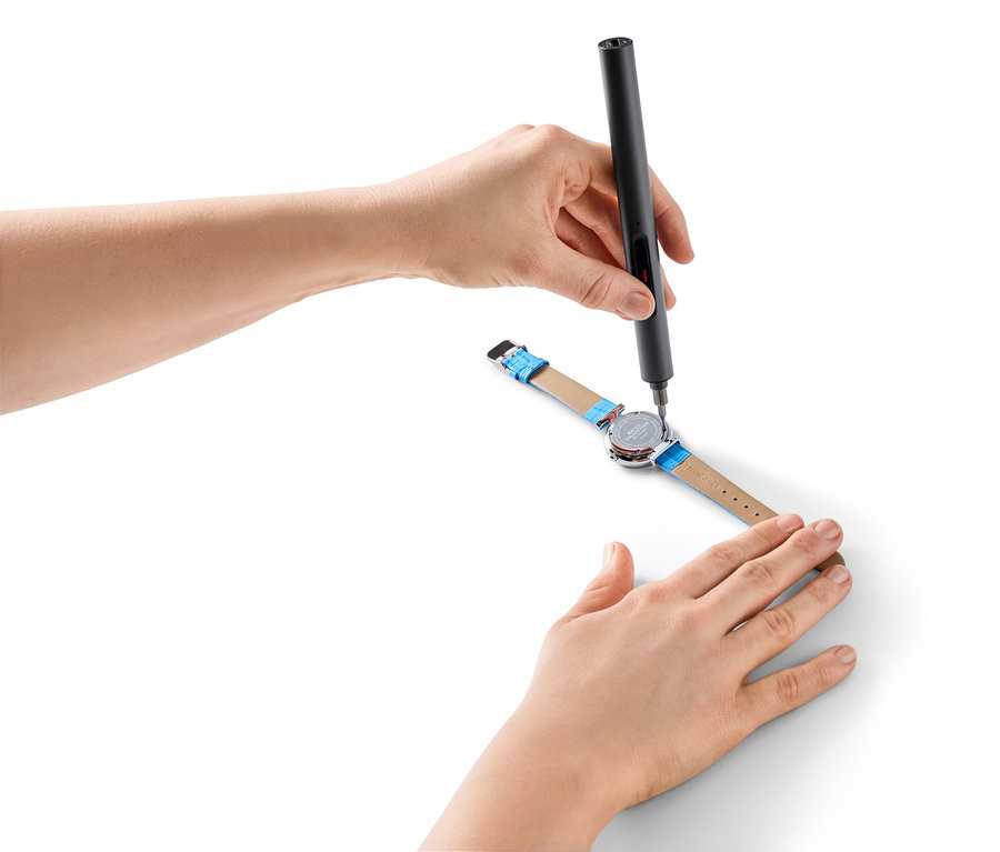 Hände benutzen ein Mini-Akku-Schraubendreher-Set, um eine Uhr zu reparieren.