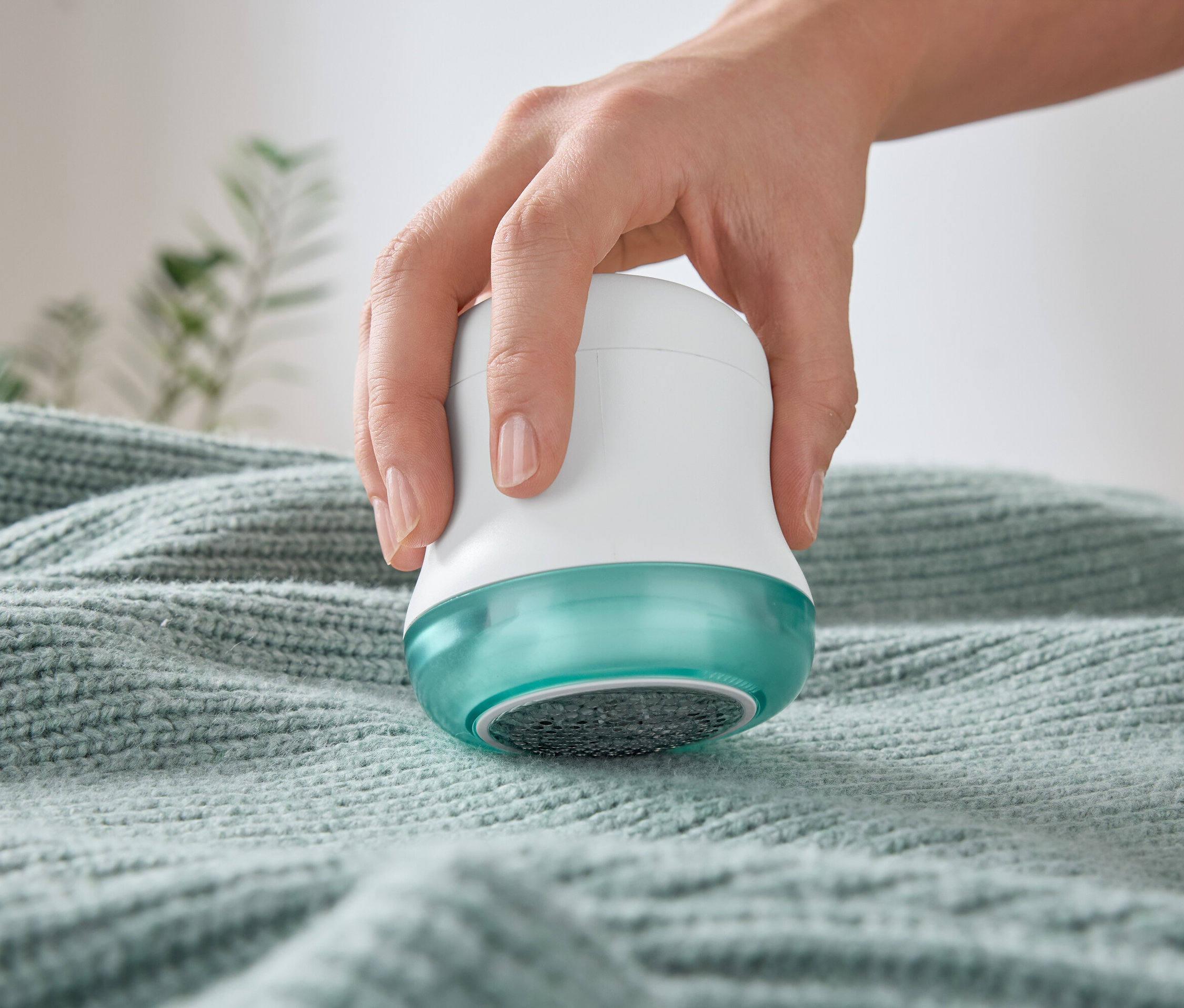 Eine Hand benutzt einen Fusselentferner auf einem Pullover.