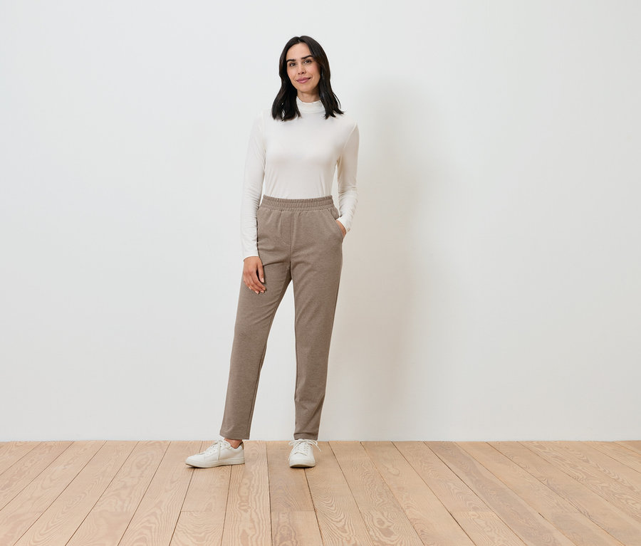 Eine Frau posiert in einem cremefarbenen Rollkragenpullover und braunen Hosen.