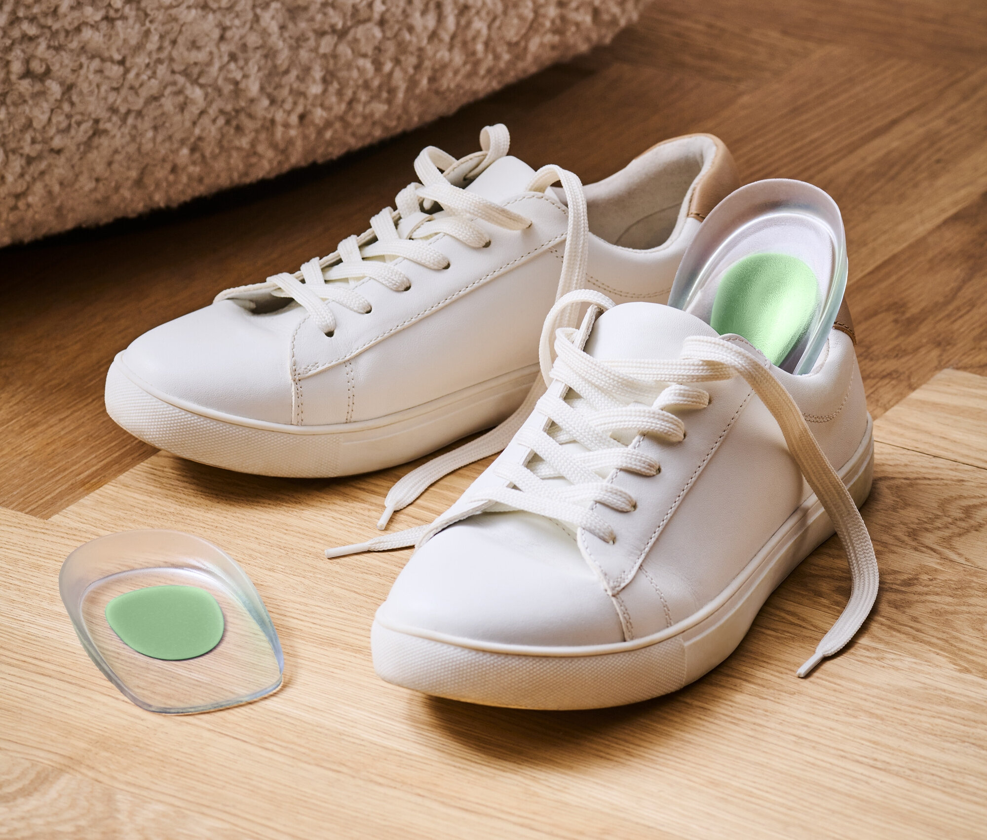 Zwei weiße Turnschuhe stehen auf einem Holzboden, einer mit einer grünen Einlegesohle.