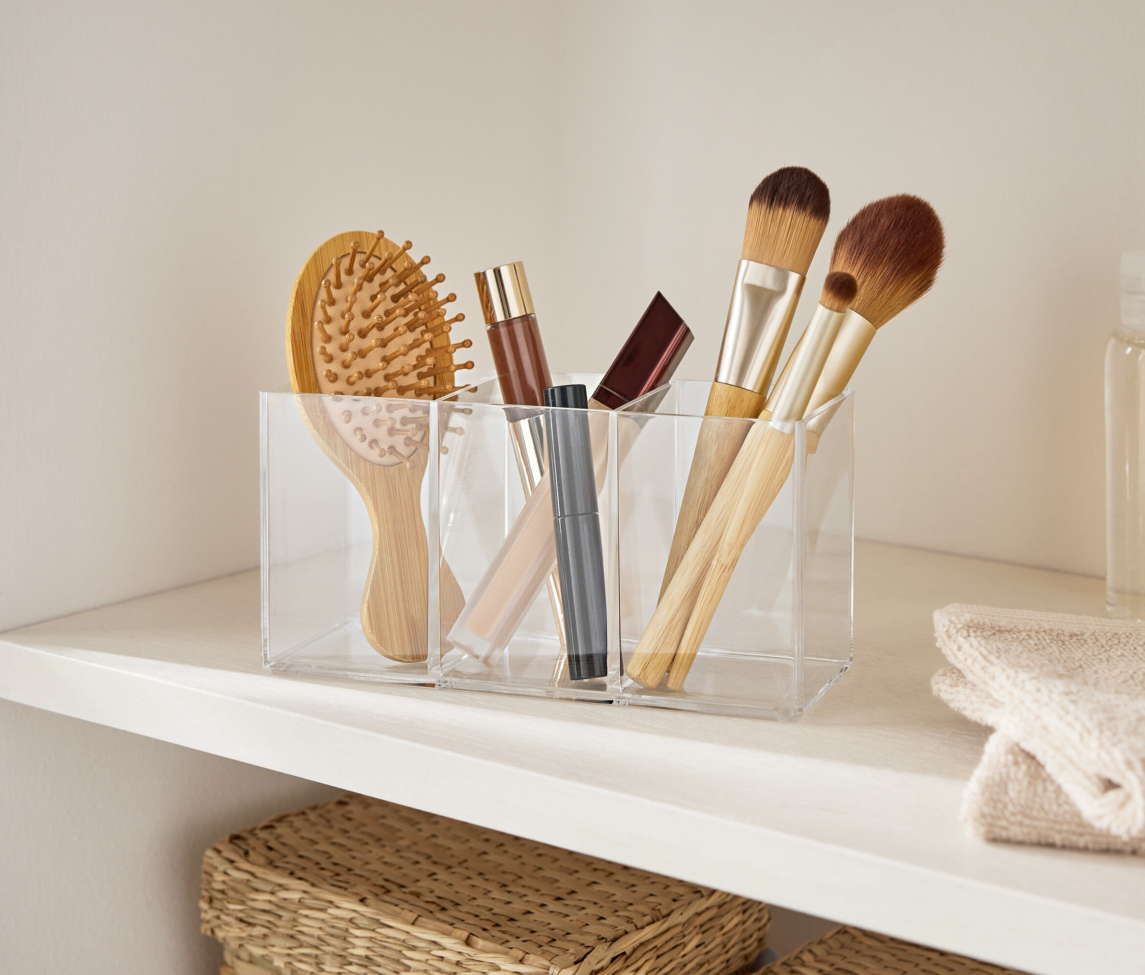 Haarbürste und Make-up-Pinsel in einem durchsichtigen Acryl-Organizer auf einem weißen Regal.