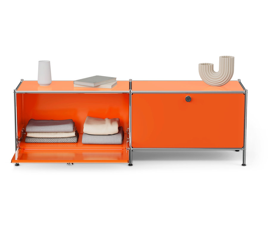 Orangefarbenes Lowboard »CN3« mit zwei Klappenfächern, eines davon offen mit gefalteter Kleidung, Vase und Bücher daneben.