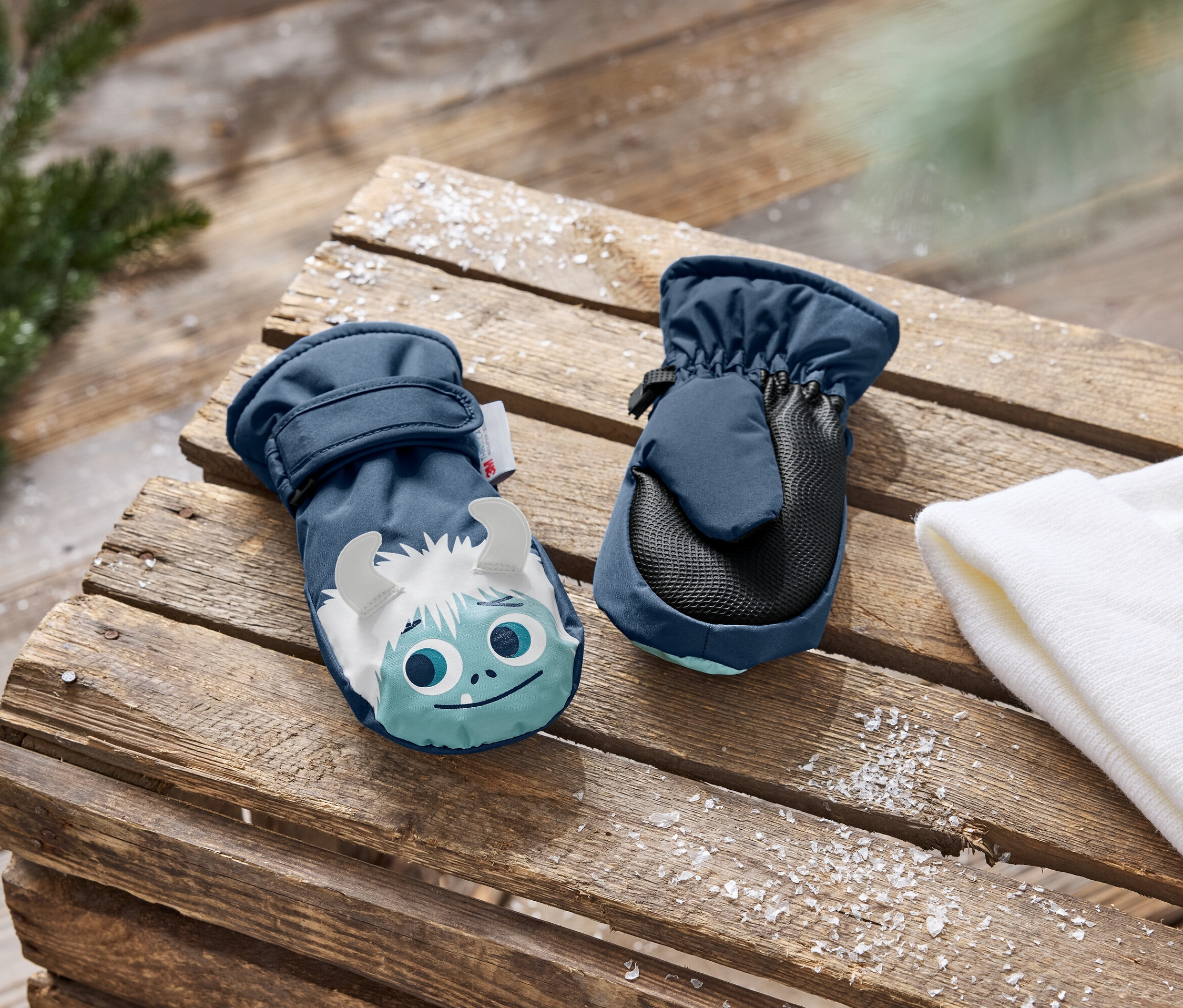 Zwei marineblaue Kinderfäustlinge mit Schneemann-Aufdruck auf einem Holzuntergrund.