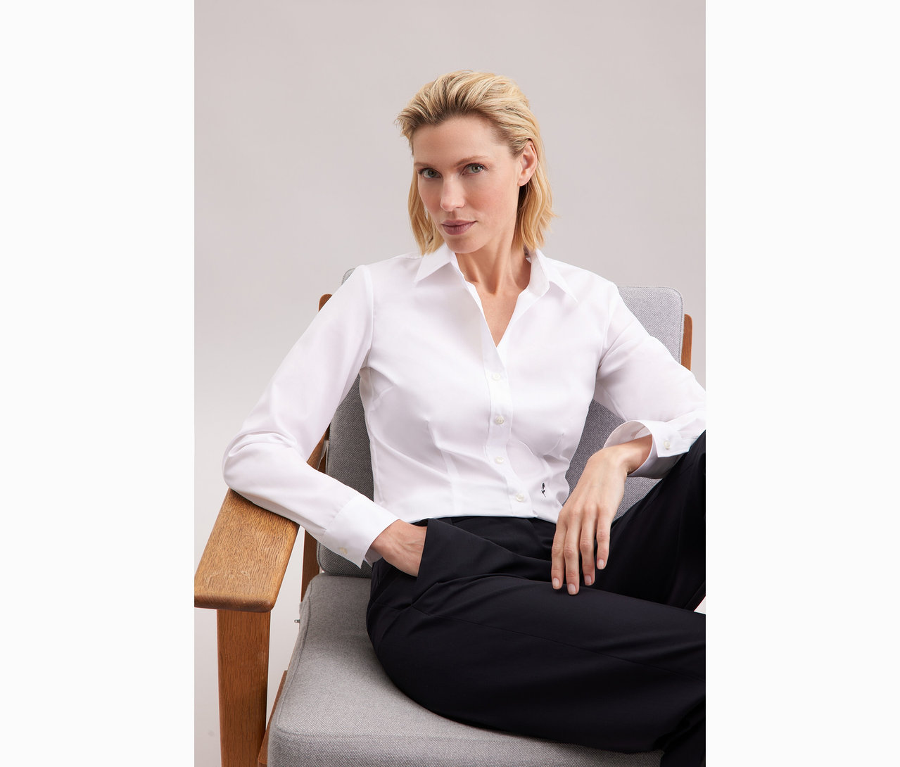 Frau sitzt in einem Stuhl und trägt eine weiße Seidensticker Bluse Slim Fit non iron.